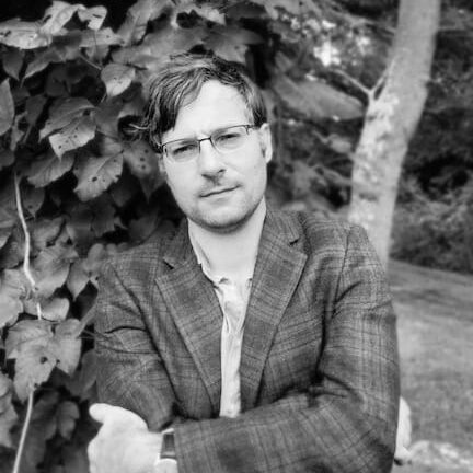 The author standing outside with arms crossed in front of a bush.